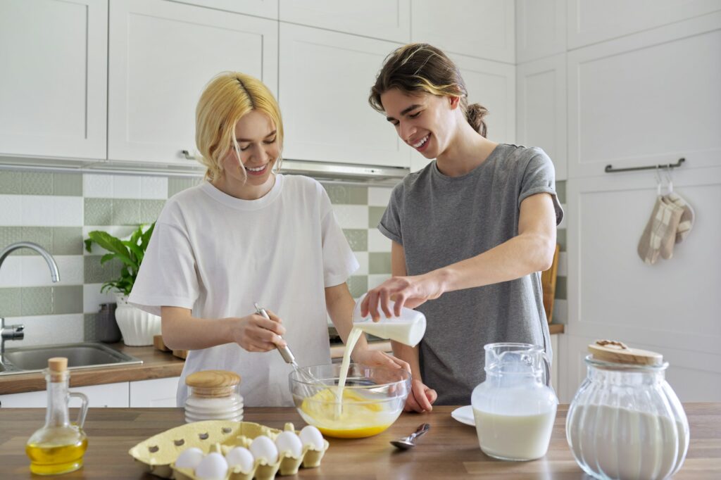 Teenagers guy and girl cooking pancakes in kitchen together