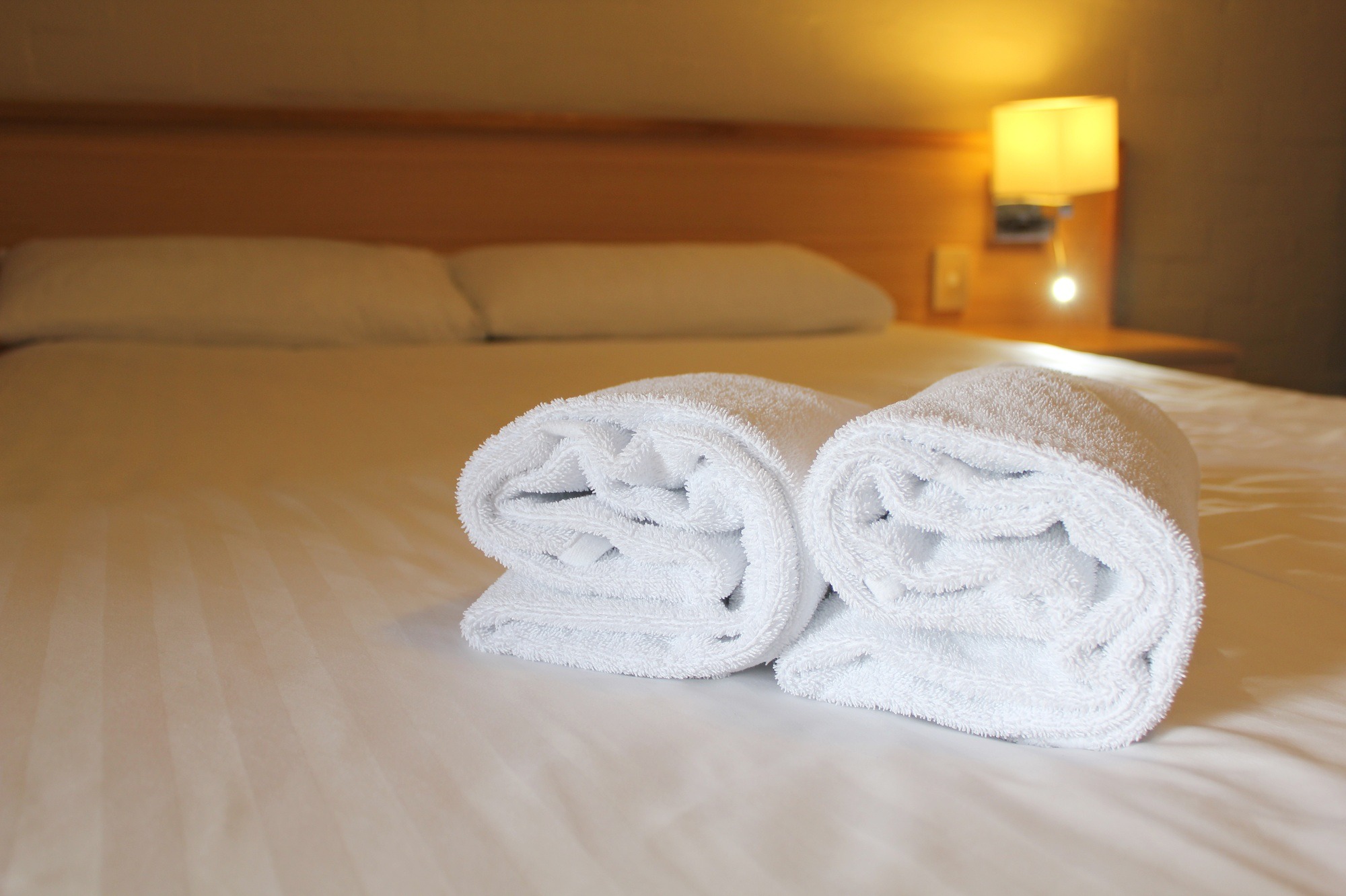 Bedside lamp, pillows and hotel room bed with fresh towels laid out