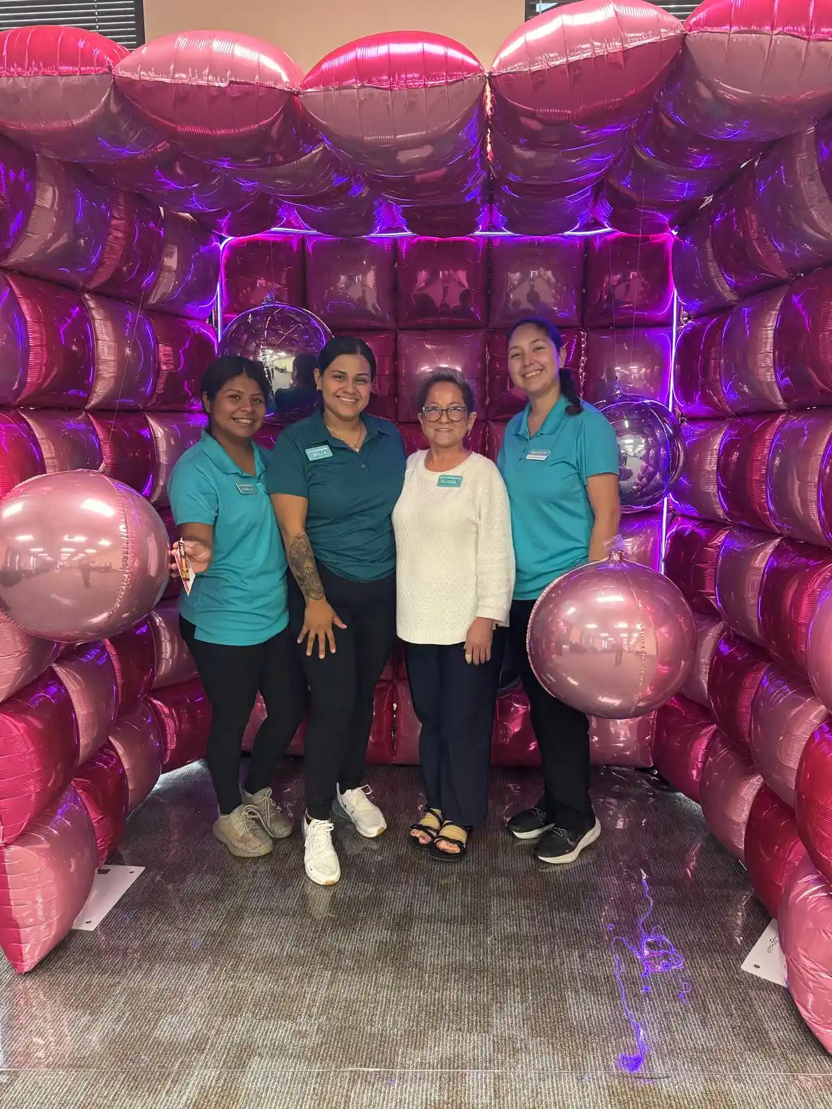 Four cleaning team members posing inside a pink balloon display at a business event in Austin