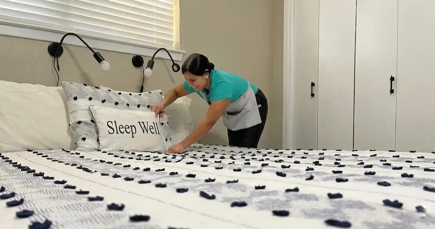 House cleaner arranging pillows on a neatly made bed in a residential bedroom in Austin