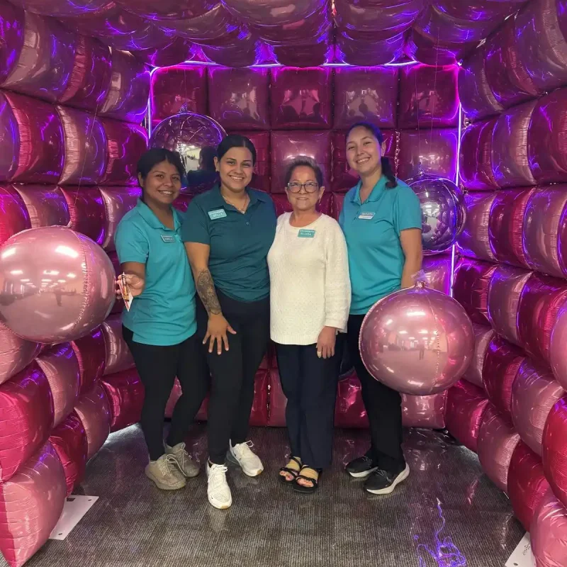 Four cleaning team members posing inside a pink balloon display at a business event in Austin